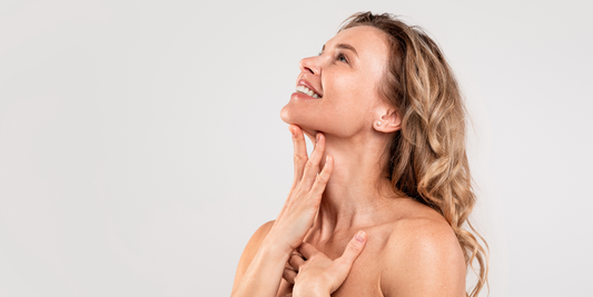 A confident older curly blonde haired woman smiling, looking up, touching her face, embracing herself and life