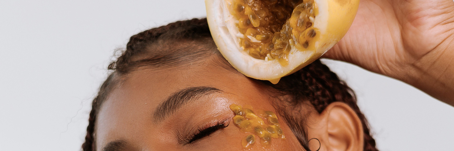 Close up of woman holding a piece of fruit and squeezing the fruit seeds onto her skin