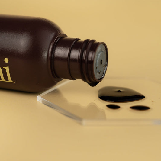 Image of he-shi Express Liquid Tan bottle on its side with the liquid product spilling onto a glass plinth to show the texture of the product
