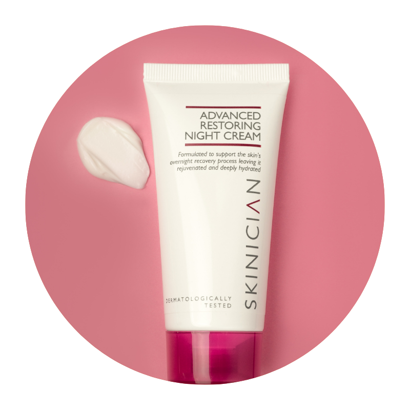 Round image of Skinician Advanced Restoring Night Cream tube lying on a red background with the cream texture beside it to demonstrate the creamy nature of the moisturiser