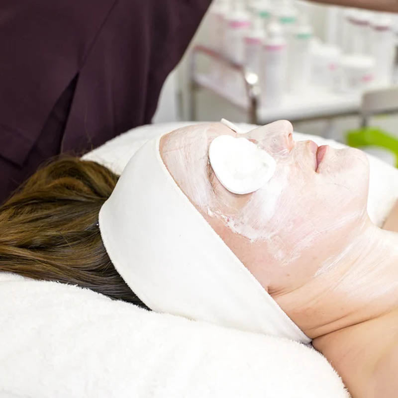 Woman with cotton rounds placed on her eyes is receiving a professional facial treatment