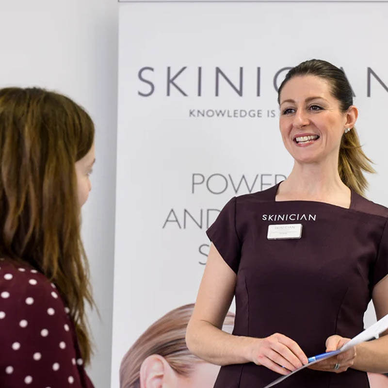Image of a Skinician skincare educator wearing a Skinician uniform is taking a client through the skincare consultation form process