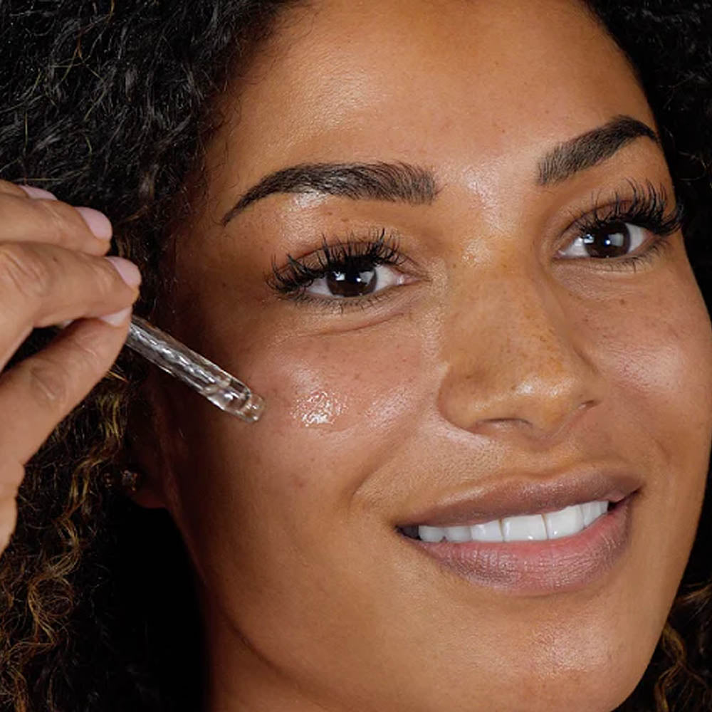 Image of woman smiling and applying Skinician Hyaluronic Elxir to her face a using a pipette
