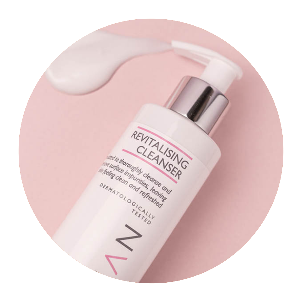Round image of Skinician Revitalising Cleanser bottle lying on its side on a light pink background with the cleanser product pouring out