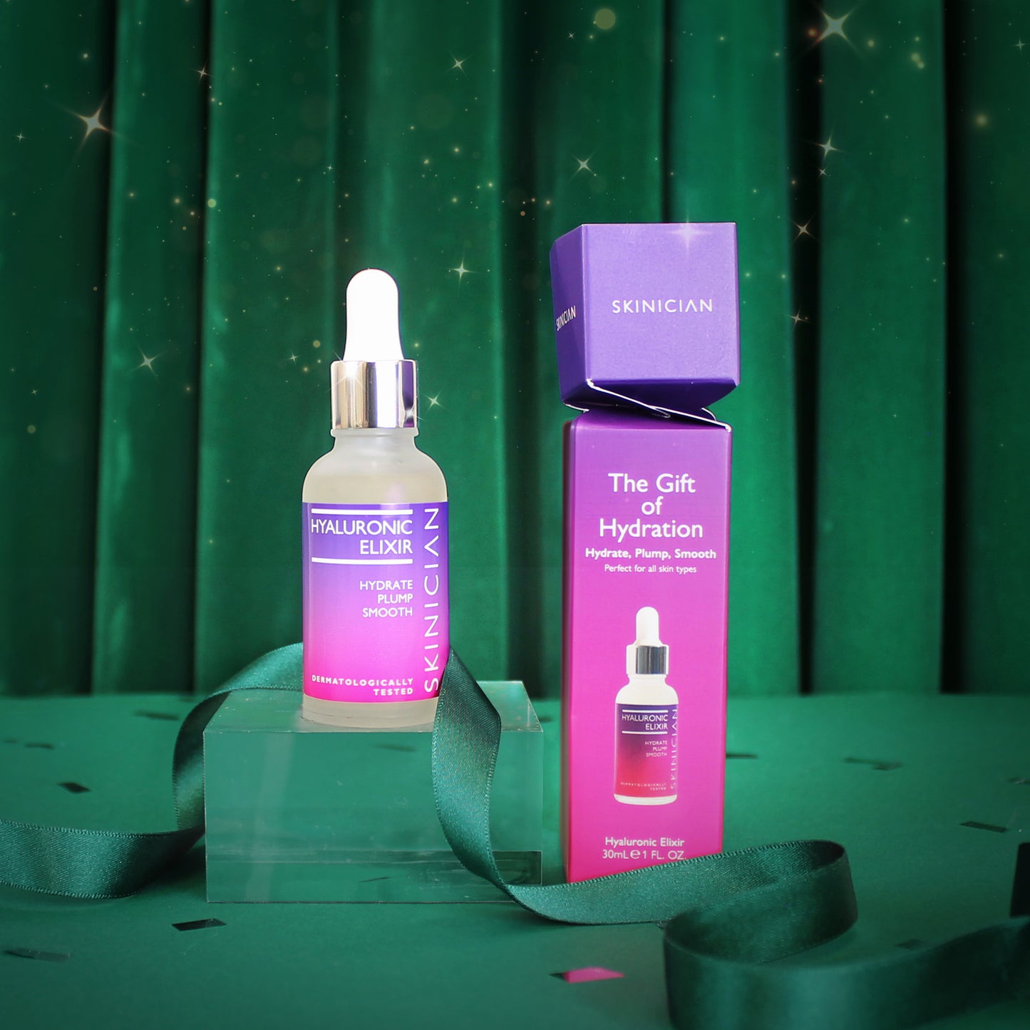 Skinician Hyaluronic Elixir bottle set beside Christmas cracker packaging on a Green velvet Christmas backdrop with green ribbon