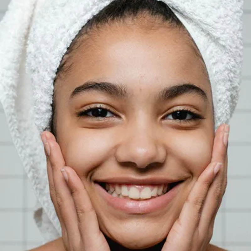 Image of young girl with a towel wrapped round her head smiling and holding her hands to her face