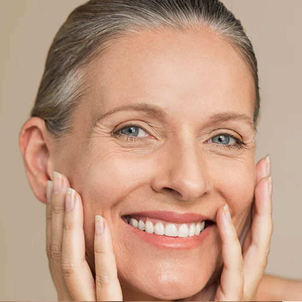 Middle-aged woman with radiant skin smiling and gently holding her face with both hands