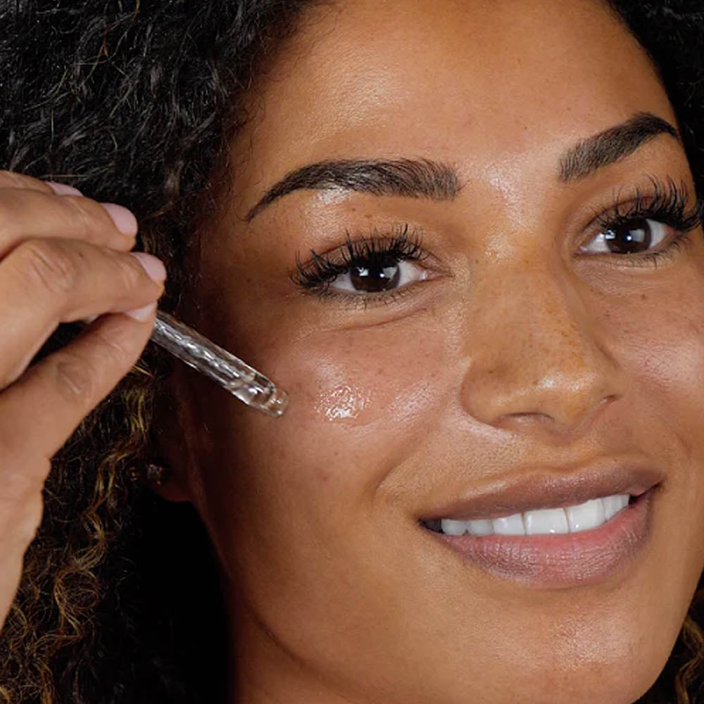 Smiling woman applying facial serum under her eye using a dropper