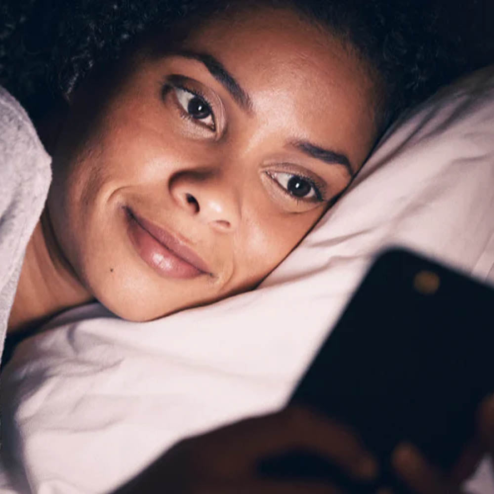 Woman lying in bed at night, smiling while looking at her phone screen.