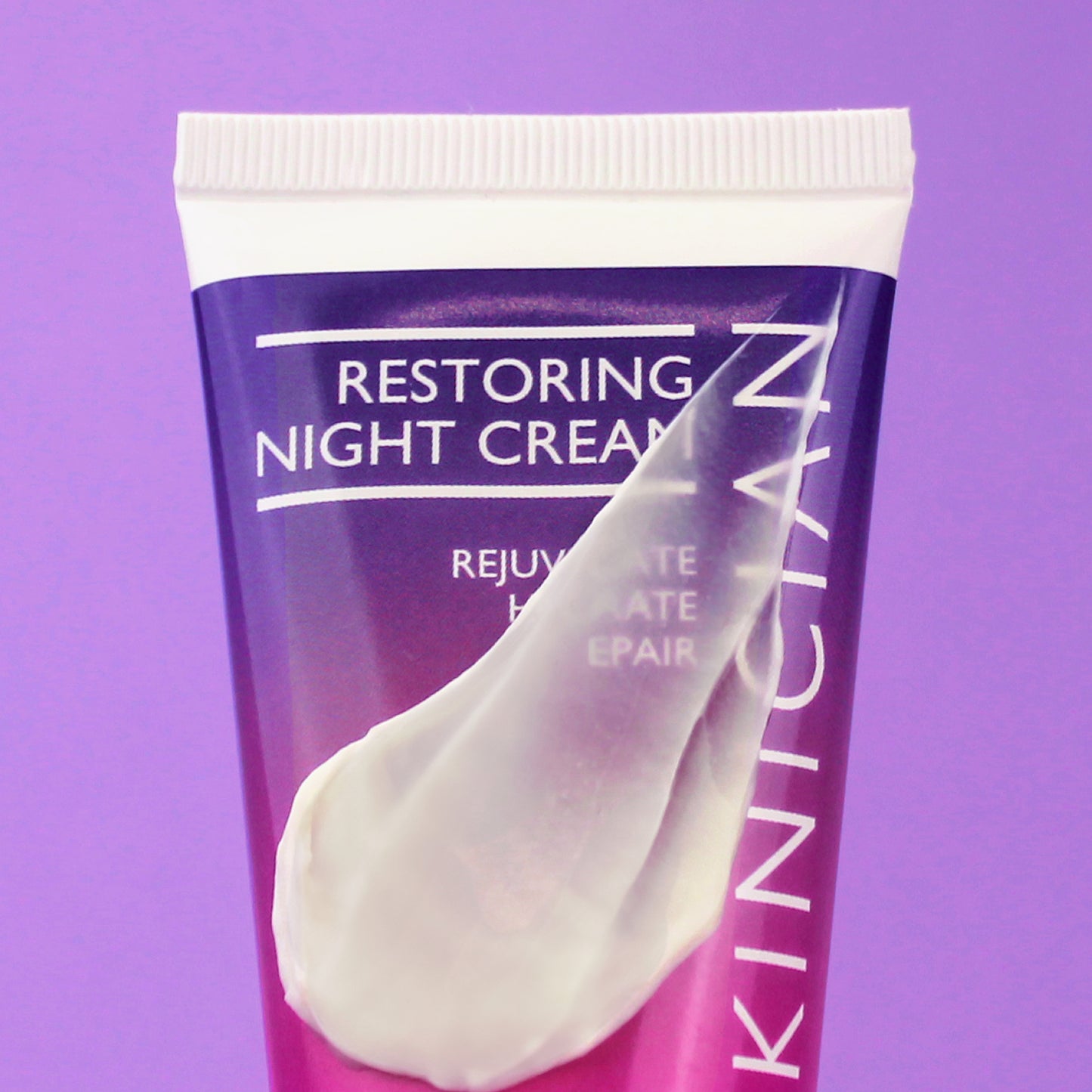 Skinician restoring night cream tube on a purple background with the product swatched on the tube to show the creamy texture