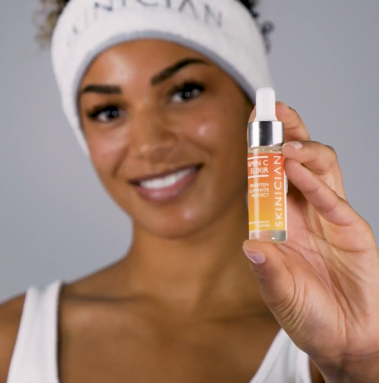 Vitamin C Elixir YouTube video, showing a lady apply the oil onto her face and blend into the skin with her fingertips. Results in 4 weeks with oranges is overlayed as text.