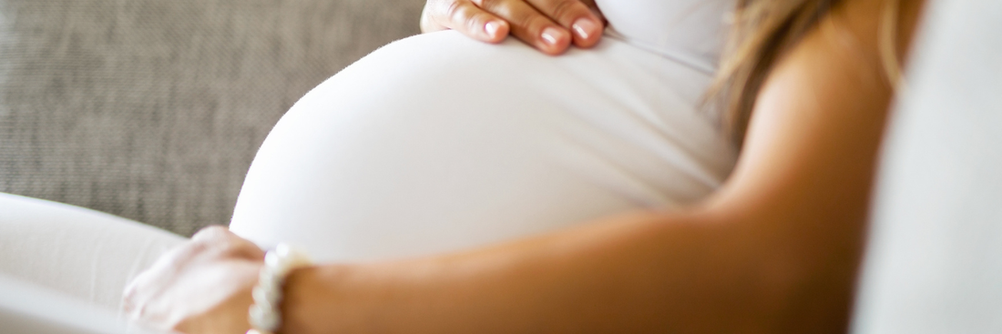 Clost up image of a woman in a white top, with her hands pressed on her pregnancy bump