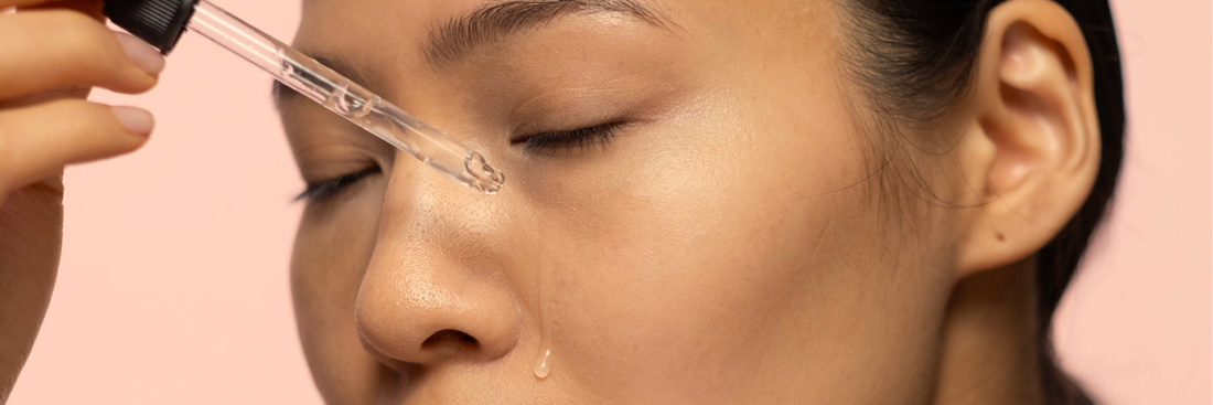 Close up of a woman holding a pipette of hyaluronic acid and dropping serum onto the face