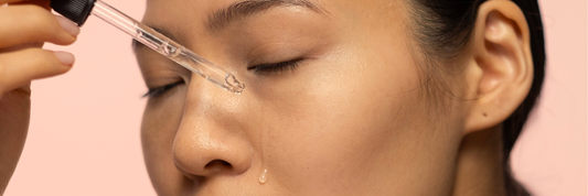 Close up of a woman holding a pipette of hyaluronic acid and dropping serum onto the face