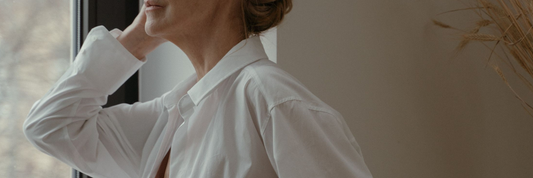 Close up image of an older woman looking out the window wearing a white shirt in front of a neutral backdrop