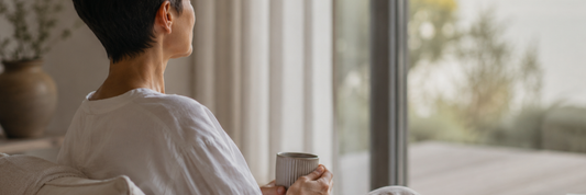 Candid image of a woman sitting at home, drinking a cup of tea, looking out the window.