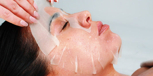 Women lying down with sheet mask being applied with professional hands