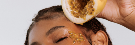 Close up of woman holding a piece of fruit and squeezing the fruit seeds onto her skin