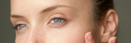 a close up of a womans face showing her blue eyes and her finger tips pressing against her cheek