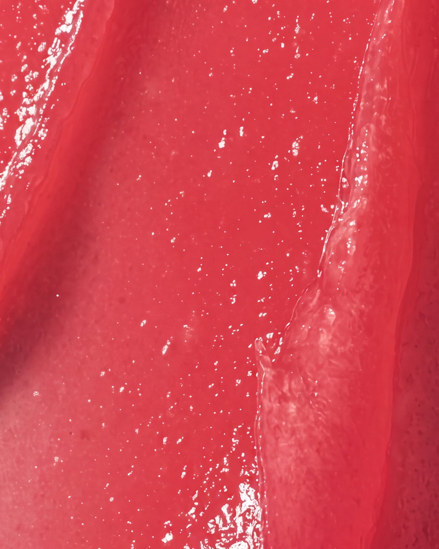 A close-up texture shot of Skinician SPF 50 + Lip Balm. It is a glossy, vibrant pinkish-red lip balm.
