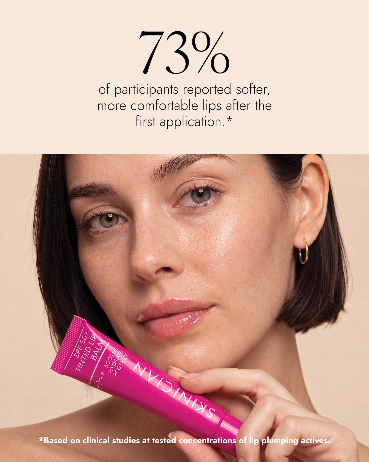 An image of a woman holding a tube of Skinician SPF 50+ Tinted Lip Balm against a warm beige background, with text above stating 73% of participants reported softer, more comfortable lips after the first applicaton.