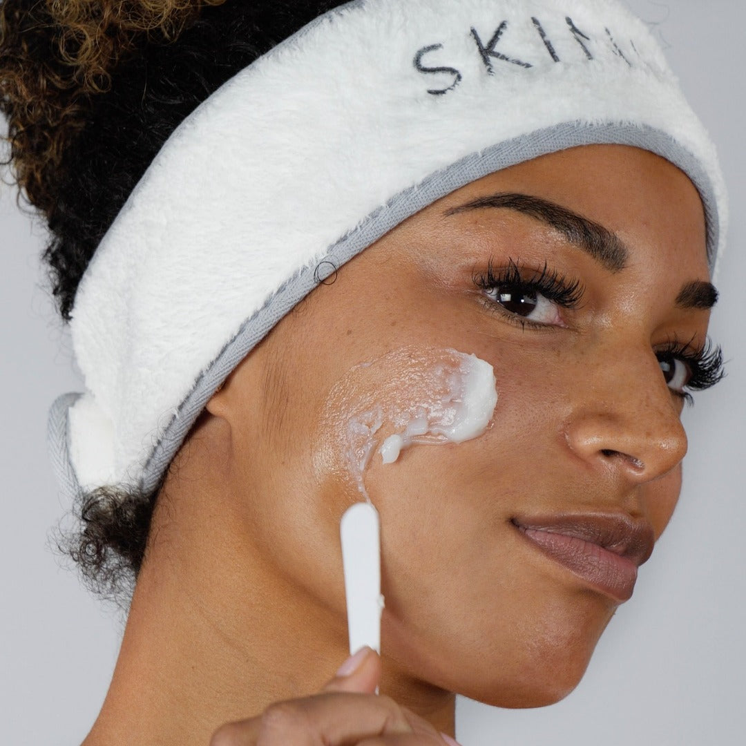 Image of a lady applying cleansing balm to her cheek, including a spatula.