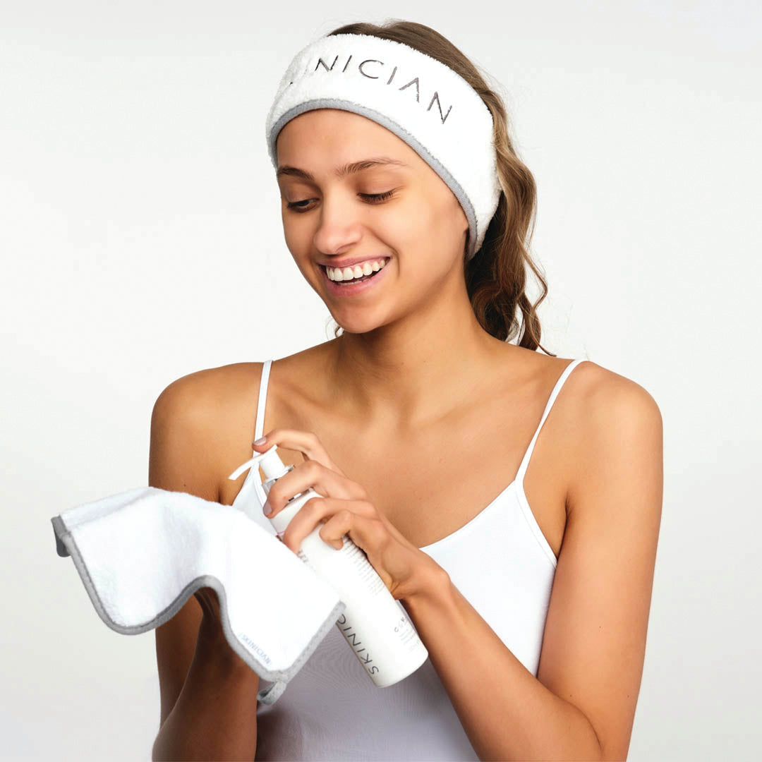 A lady with the skinician skincare band on her head and a face cloth and cleanser in her hands